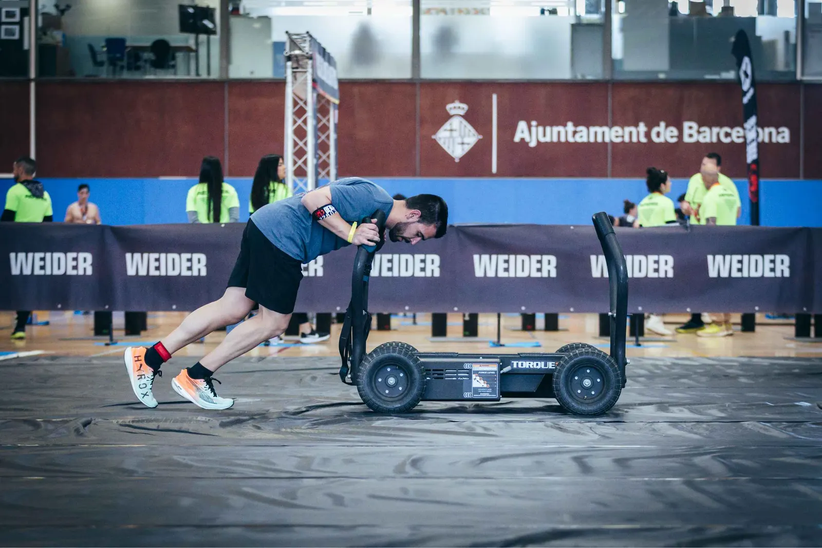 Atleta empujando un trineo frente a la pancarta del Ajuntament de Barcelona