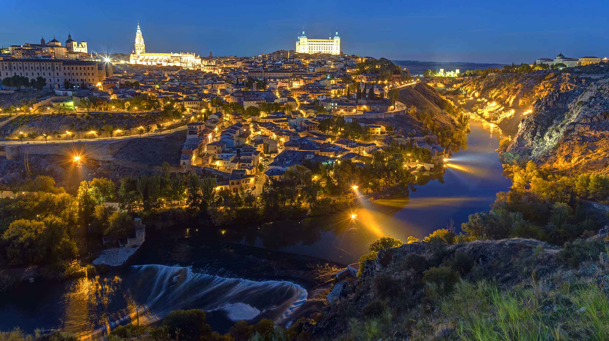 Vista nocturna del casco histórico de Toledo iluminado sobre el río Tajo, con la Catedral y el Alcázar al fondo