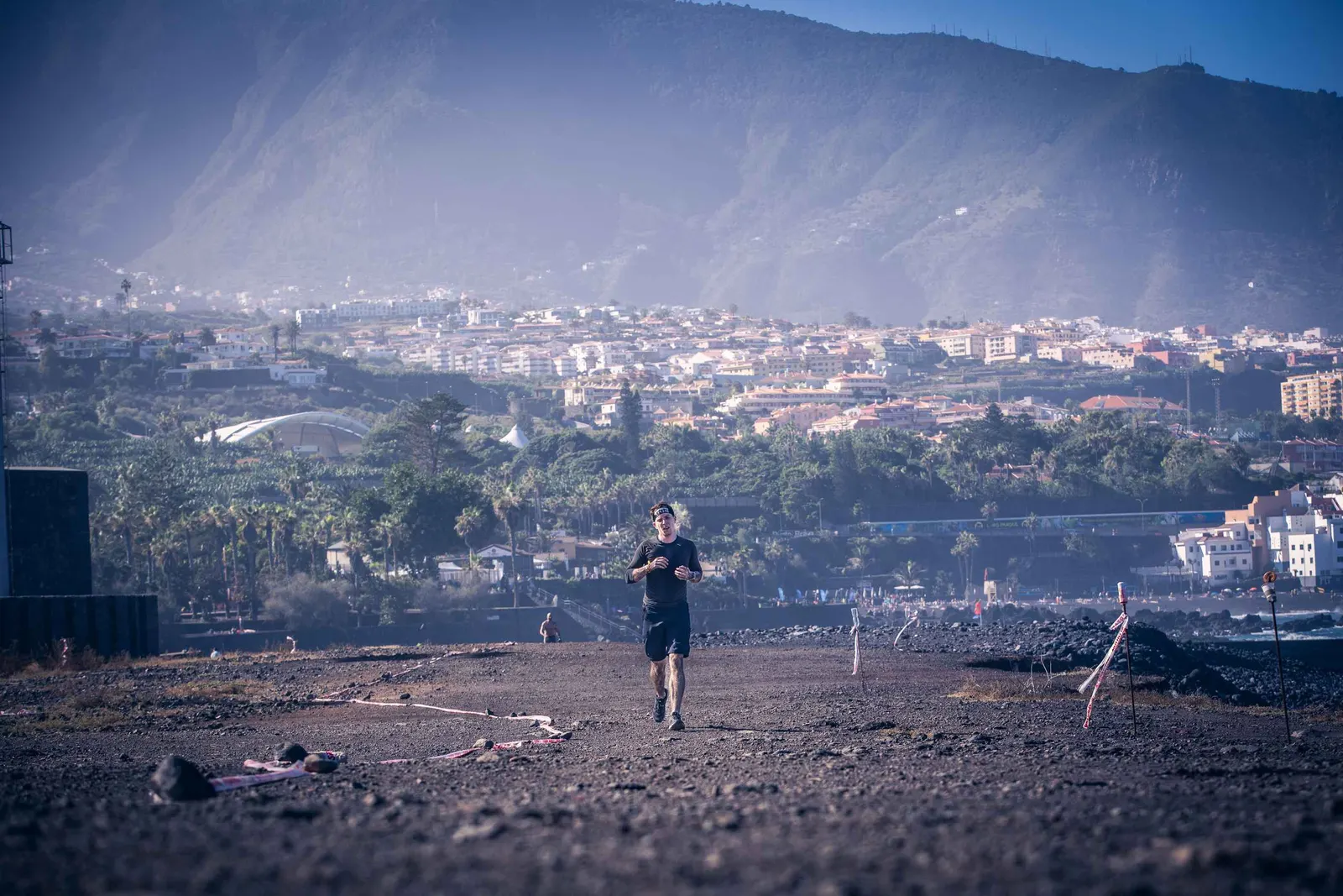 Corredor por una pista volcánica con Puerto de la Cruz y la montaña al fondo