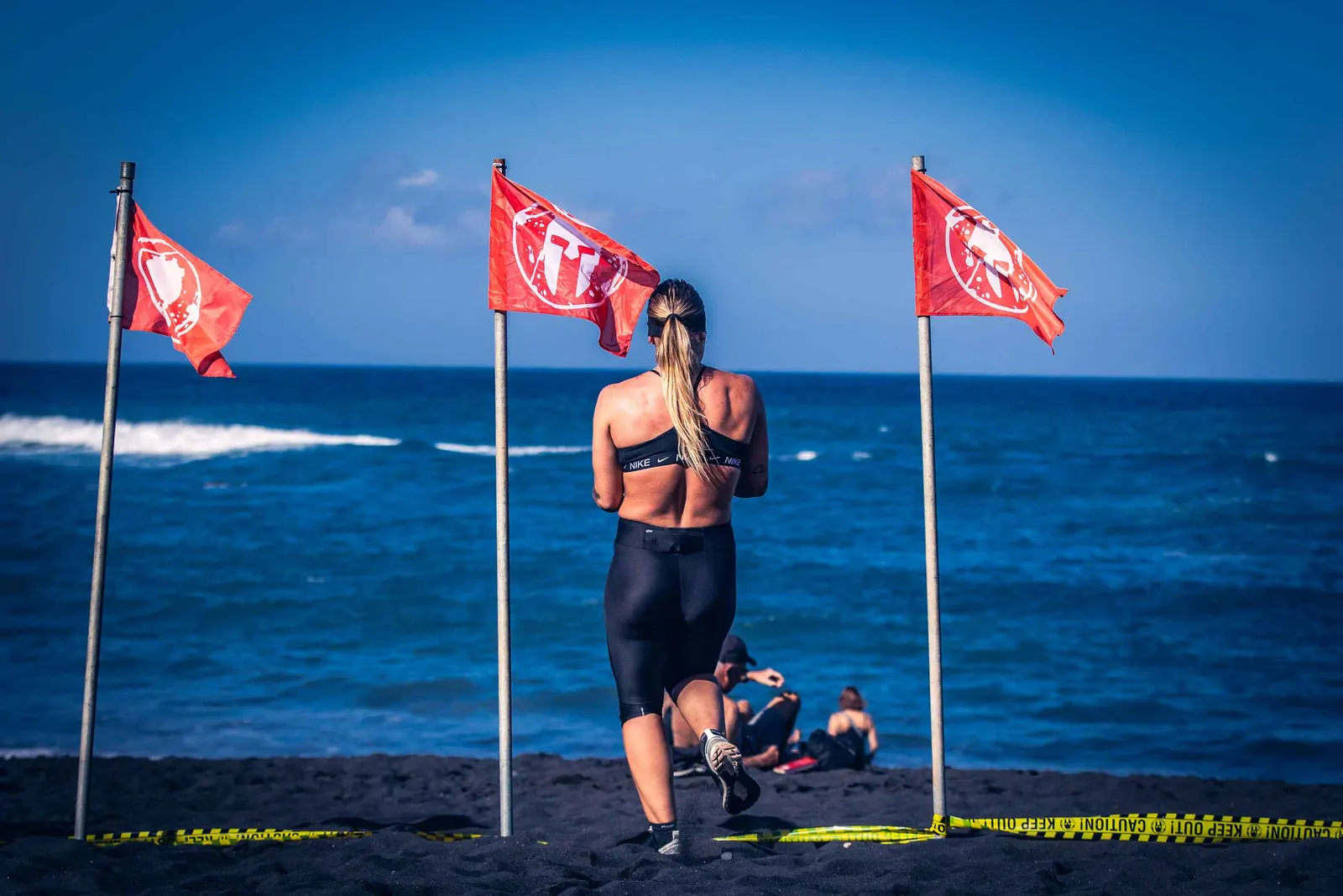 Corredora en la arena negra, entre banderas Spartan frente al Atlántico, en Puerto de la Cruz